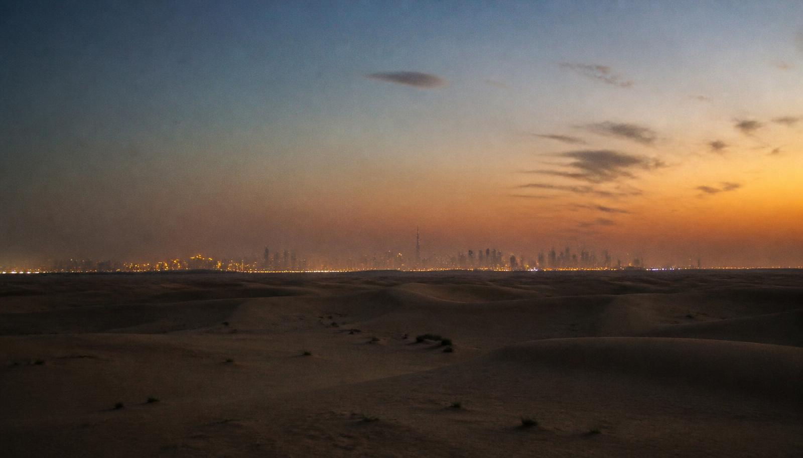 The desert edge outside Dubai at dusk, with the city lights on the horizon
